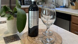Eine Küchenarbeitsplatte mit einer Flasche Sterling Vintner's Collection Cabernet Sauvignon, einem Glas Wasser und einer Topfpflanze mit Orchideen.