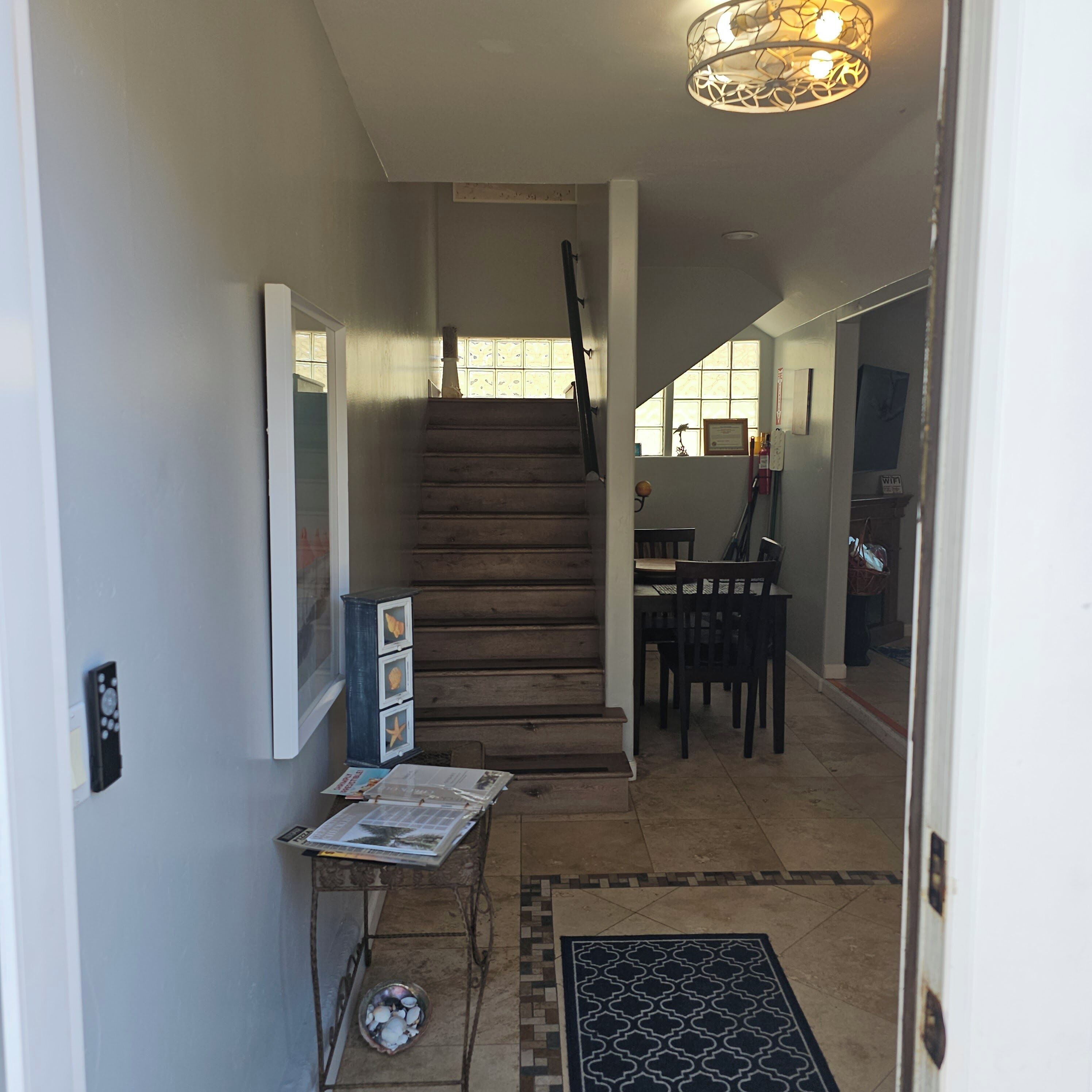 A staircase leading to a dining area with a table and chairs, a wall-mounted light fixture, and a small cabinet with decorative items.