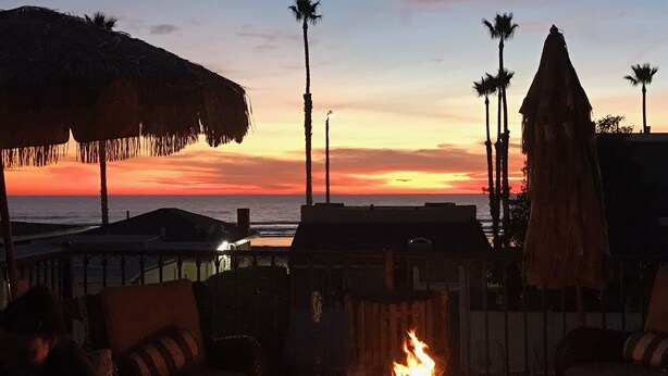 Ein Sonnenuntergangsblick vom Strand, mit Liegestühlen, einer Feuerstelle und Palmen.