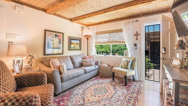 A cozy living room with a grey sofa, patterned armchairs, a large rug, and a window with a view of greenery. - So. Capitol area quaint casita! Walk to Railyard & Plaza (Santa Fe)