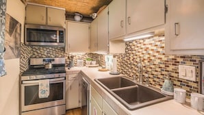 A kitchen with stainless steel appliances, a tiled backsplash, and light-colored cabinetry. - So. Capitol area quaint casita! Walk to Railyard & Plaza (Santa Fe)