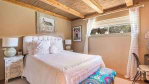 A bedroom with a large bed, wooden ceiling beams, a window with curtains, and a chair. - So. Capitol area quaint casita! Walk to Railyard & Plaza (Santa Fe)