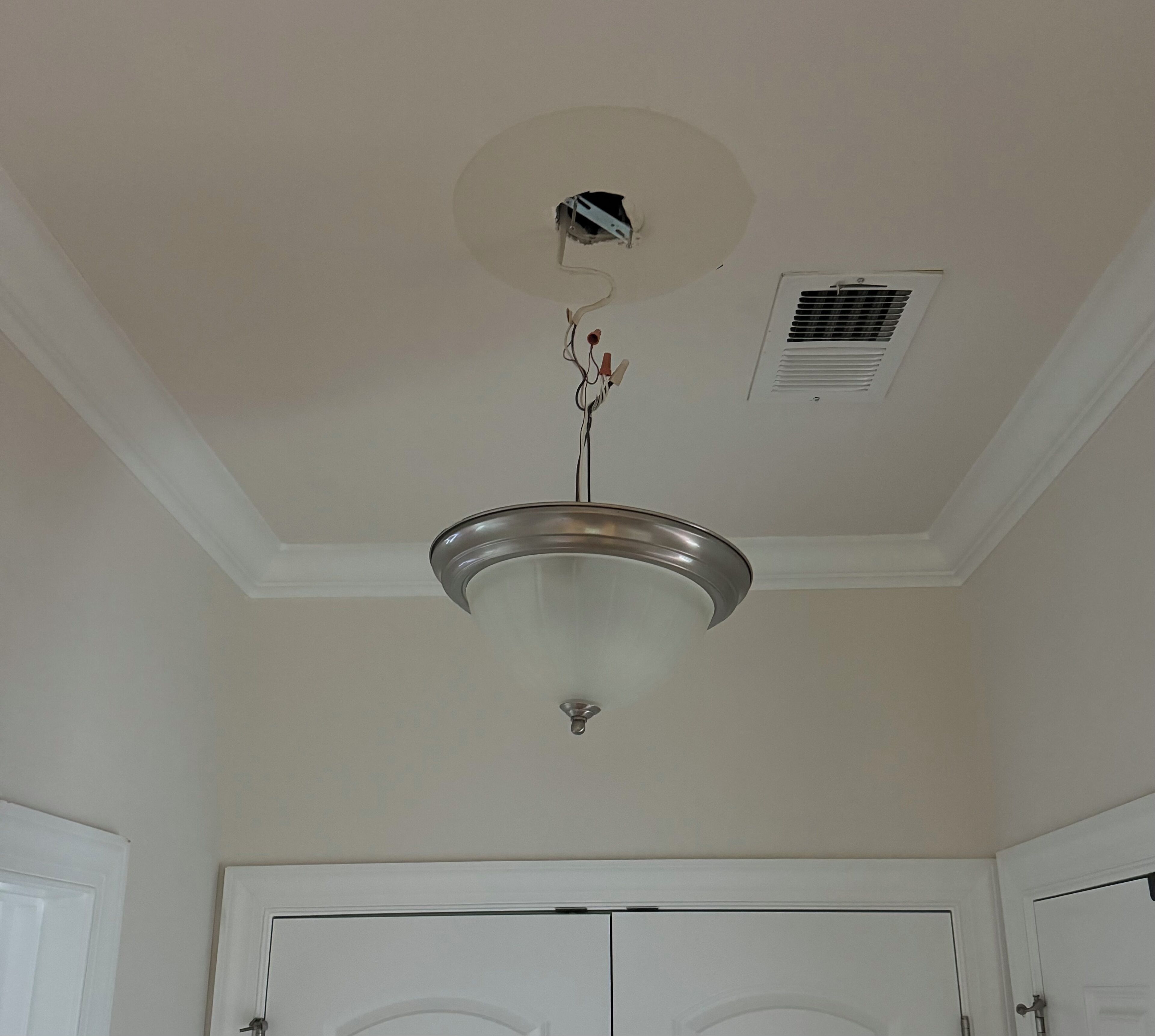A ceiling with a central light fixture, a vent, and a door below.