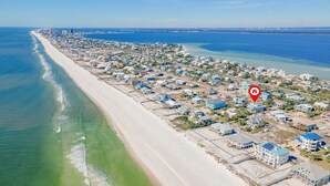 Ett flygbildsbild av ett bostadsområde vid kusten, med hus längs stranden, en pir som sträcker sig ut i vattnet och en röd markör som visar platsen.