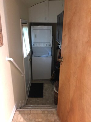 Una cocina compacta con lavadora y secadora integradas, un ventanal pequeño y una puerta que da a otra habitación.