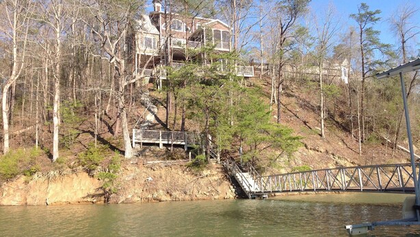 Una casa su più livelli, circondata da alberi e un ponte che scavalca un corso d'acqua.
