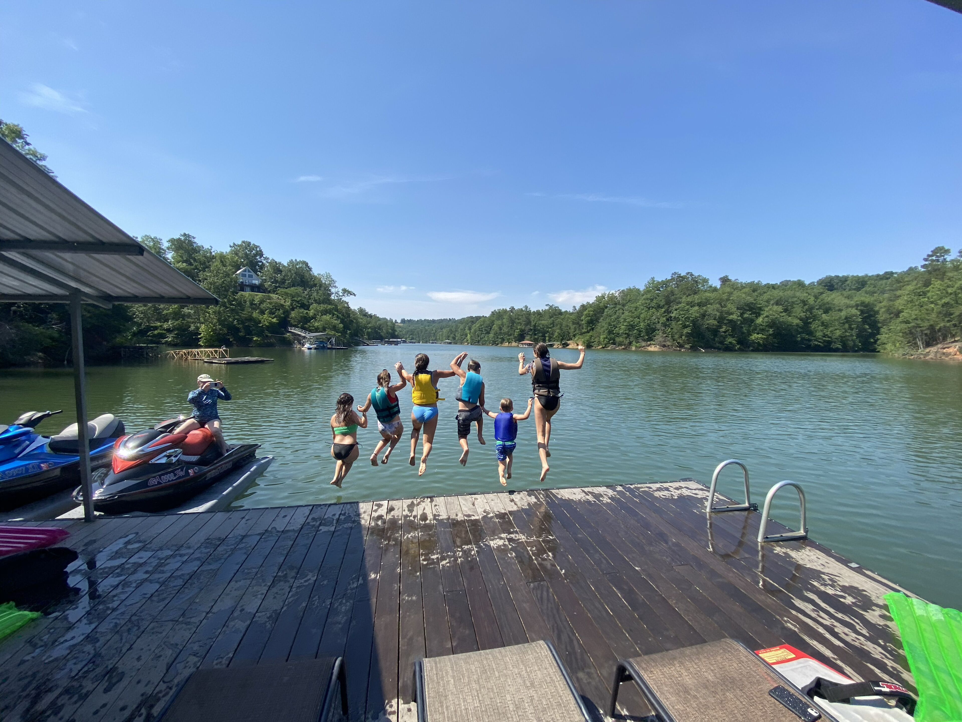 A wooden dock with a metal railing, a jet ski, and a rowboat.