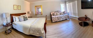 A hotel room with a large bed, a smaller sofa, a round table, and a TV on the wall. - Minutes from Morro Bay, Beaches, Montana De Oro, Wineries, Golf, Hiking (Los Osos)