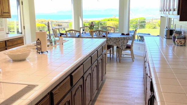A spacious kitchen with a large island, wooden cabinets, and a view of the ocean.