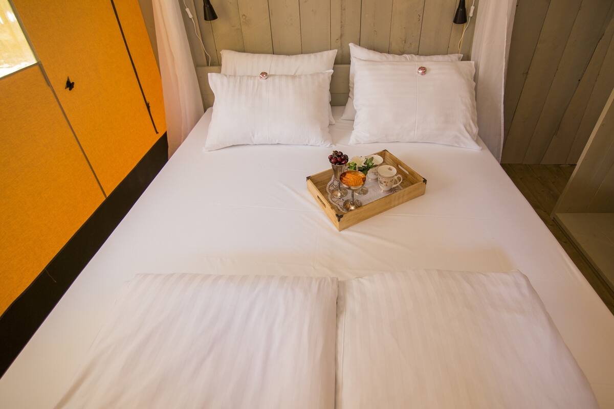 A neatly made bed with white linens, a tray with a glass of orange juice, a vase with flowers, and a teapot.