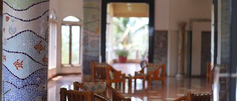 A lobby with mosaic columns, wooden chairs, and a view of the outdoors.