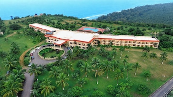 Un hotel grande con un patio central, rodeado de palmeras y vistas al mar.