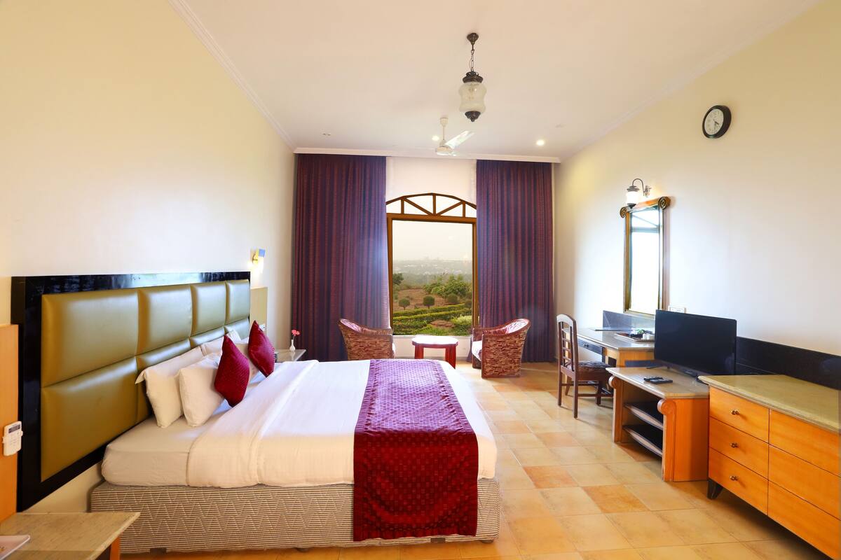 Habitación de hotel con una cama grande, un escritorio, una silla y vistas al campo.