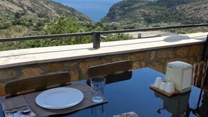 Une table à manger dressée pour deux personnes, avec vue sur la mer et les collines.