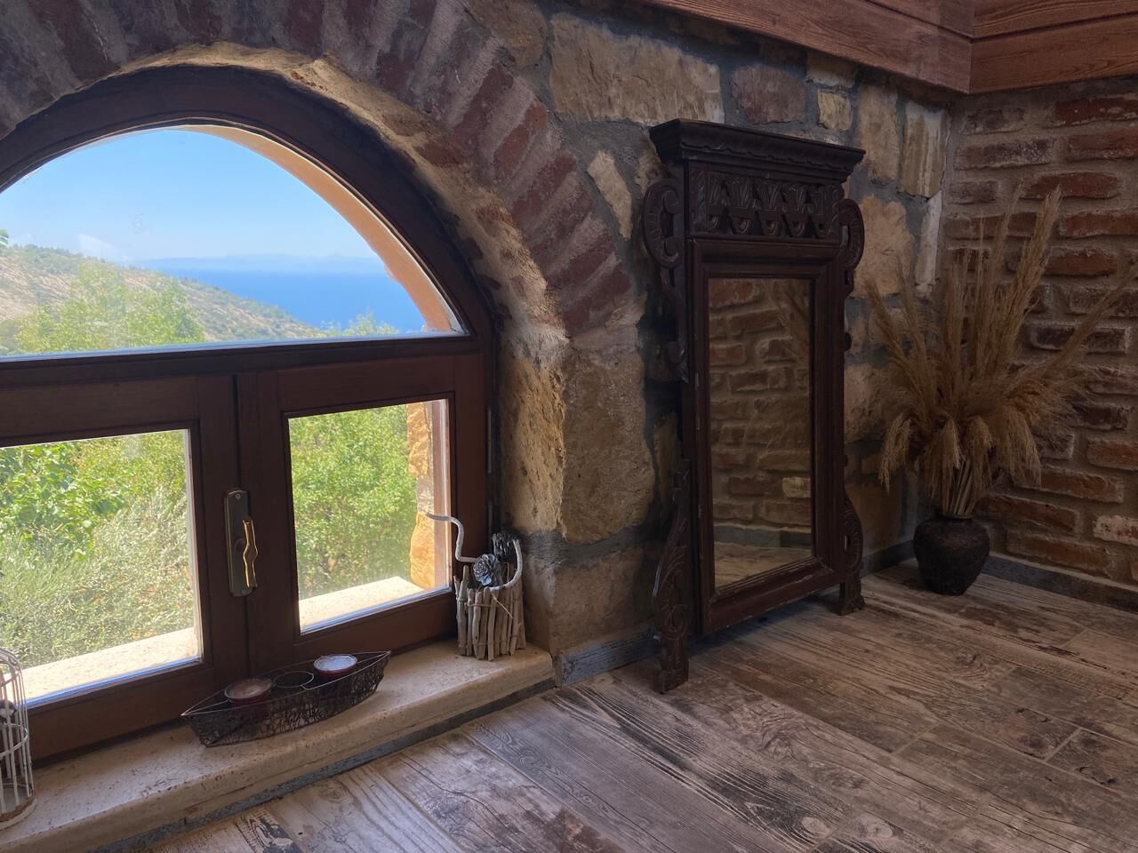 A room with a stone wall, a large arched window, a wooden floor, and a mirror.