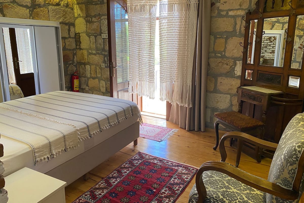Una camera da letto con un letto, una sedia in legno, una scrivania e un muro in pietra.