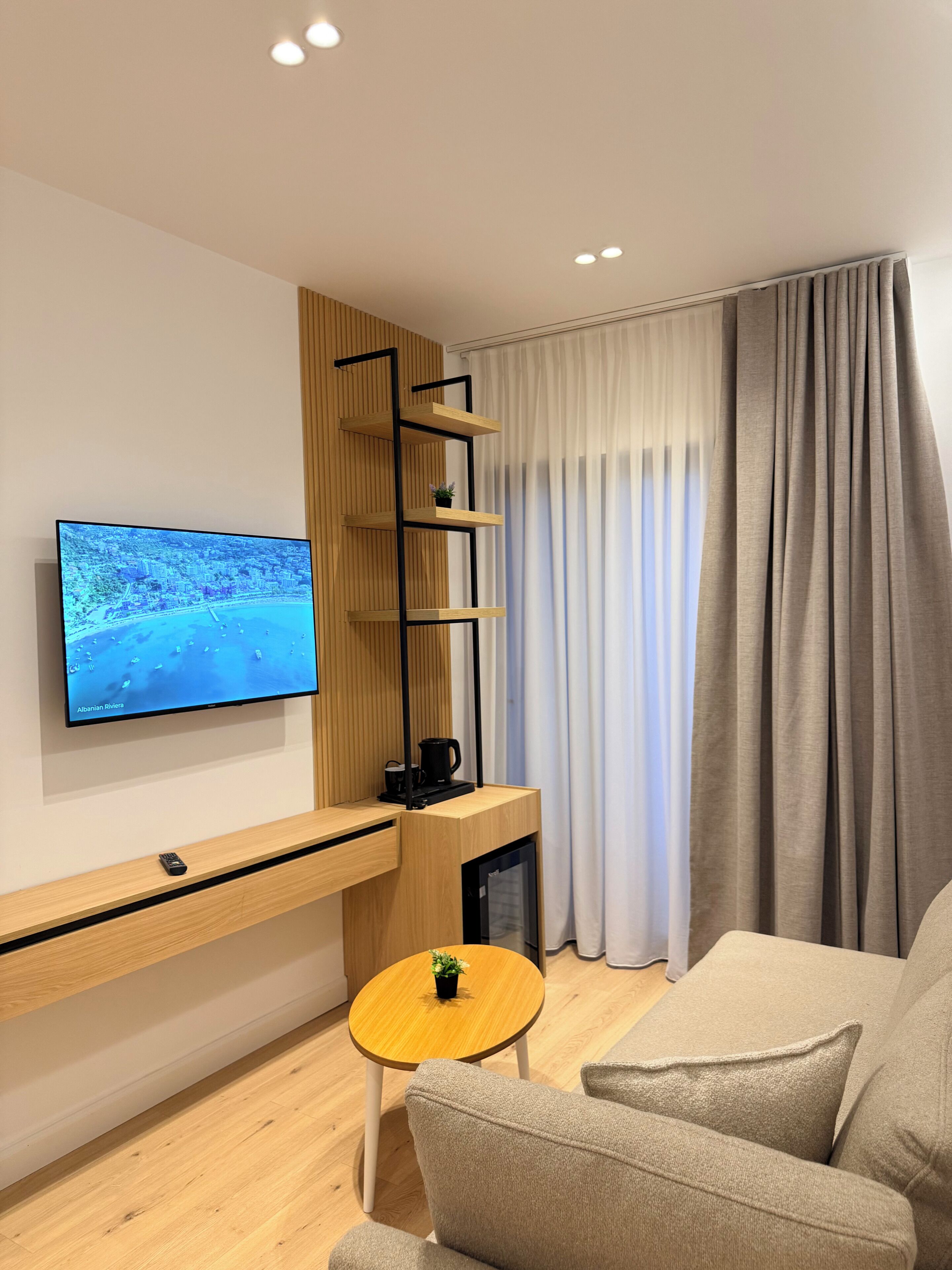Een moderne woonkamer met een flatscreen televisie, een houten tv-meubel, een klein rond tafeltje en een beige bank.