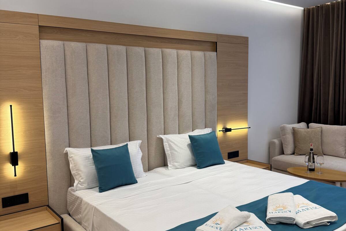 A modern hotel room with a large bed, two bedside tables, a sofa, and a minibar.