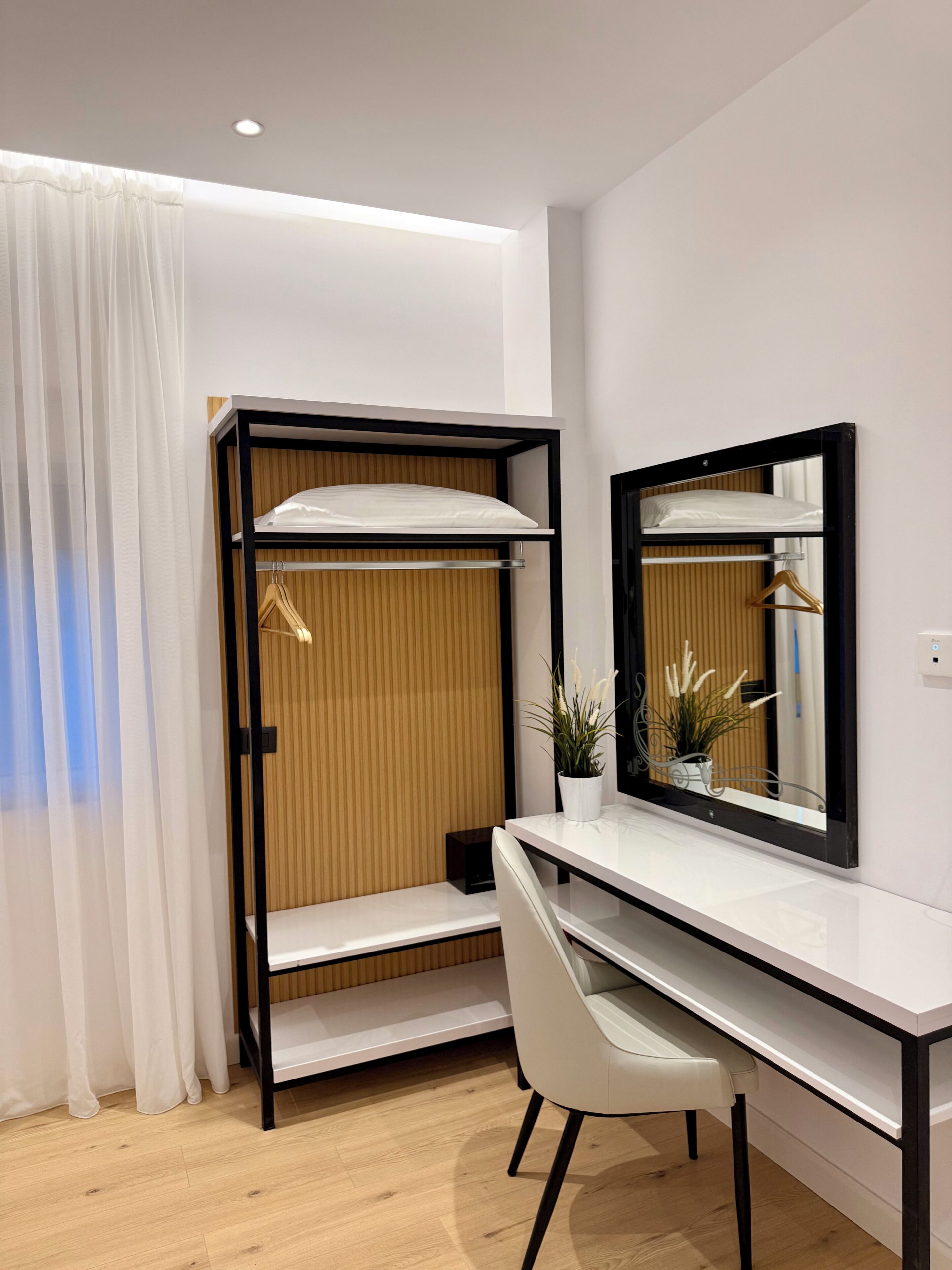 Quarto moderno com cama beliche, escrivaninha, cadeira, espelho e planta em vaso.
