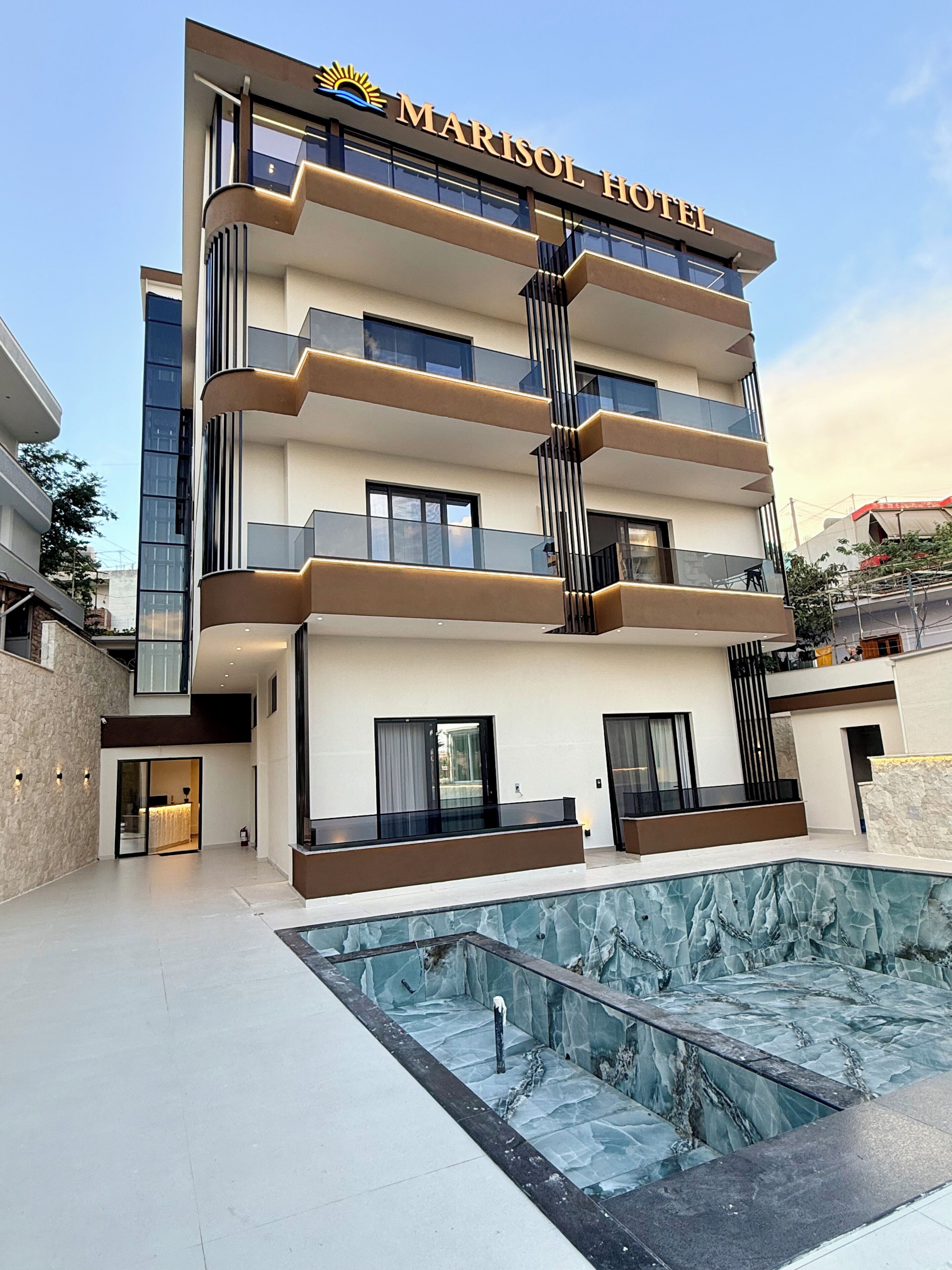 A modern Marisol Hotel with a glass facade, multiple balconies, and a swimming pool.