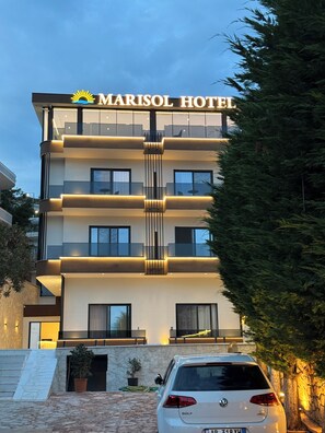 A multi-story hotel with a prominent sun logo, balconies, and a car parked in front. - Marisol Hotel (Sarandë)