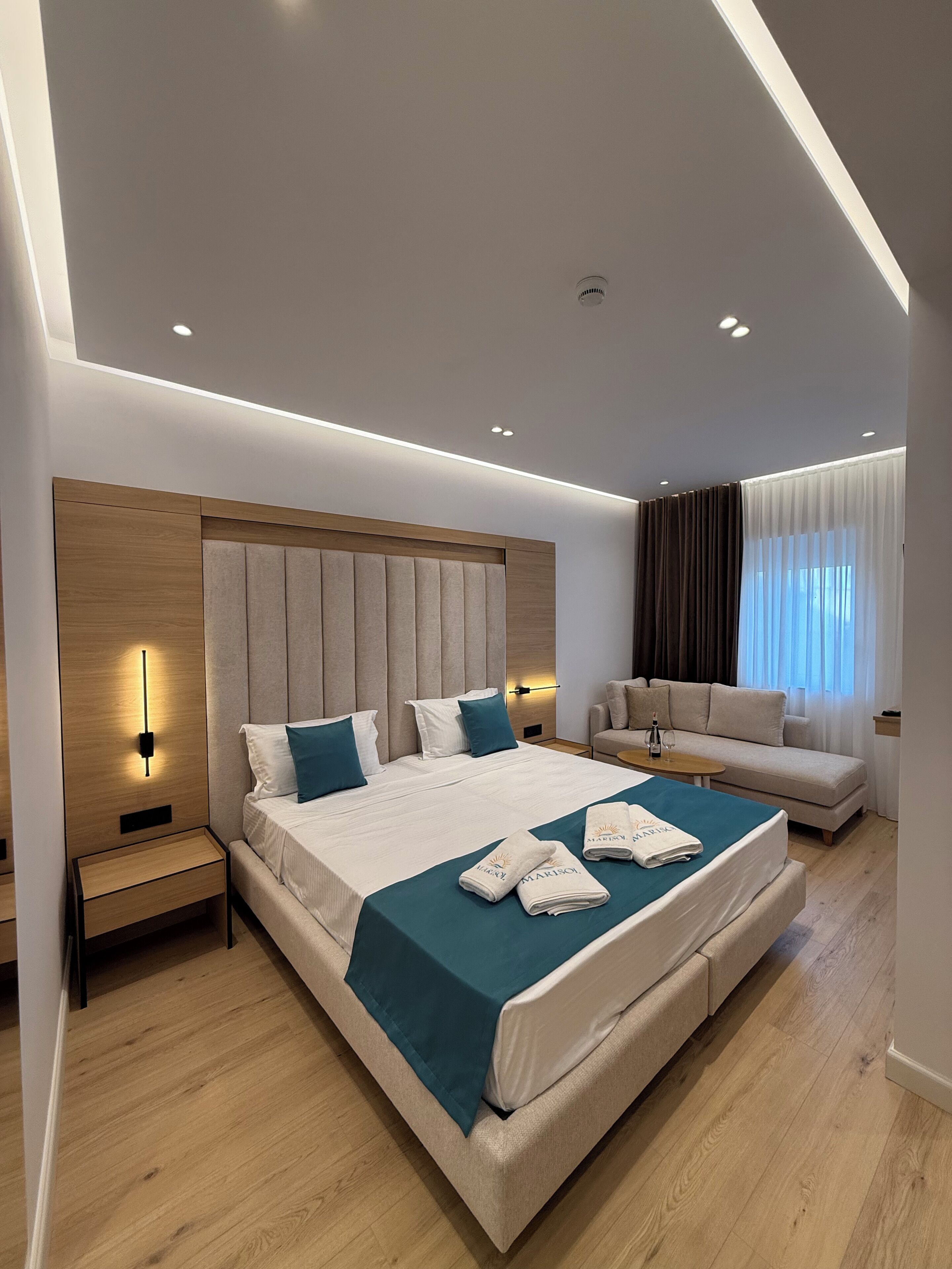 Una habitación de hotel moderna con una cama grande, un sofá, una mesita de noche y una ventana con cortinas.