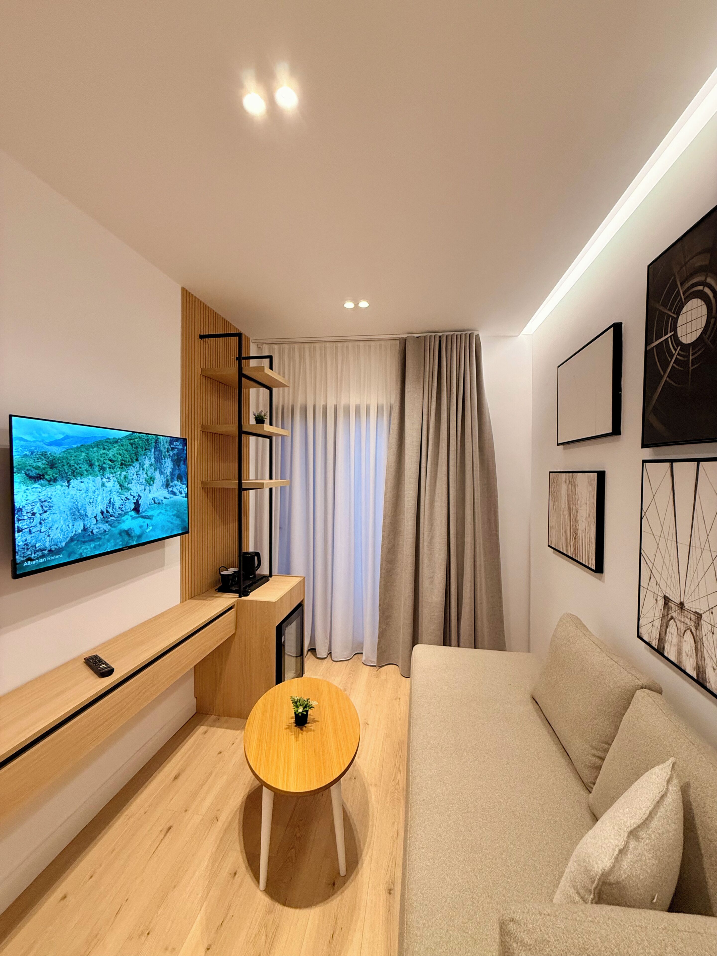 A modern living room with a flat-screen TV, wooden furniture, a sofa, and artwork on the walls.