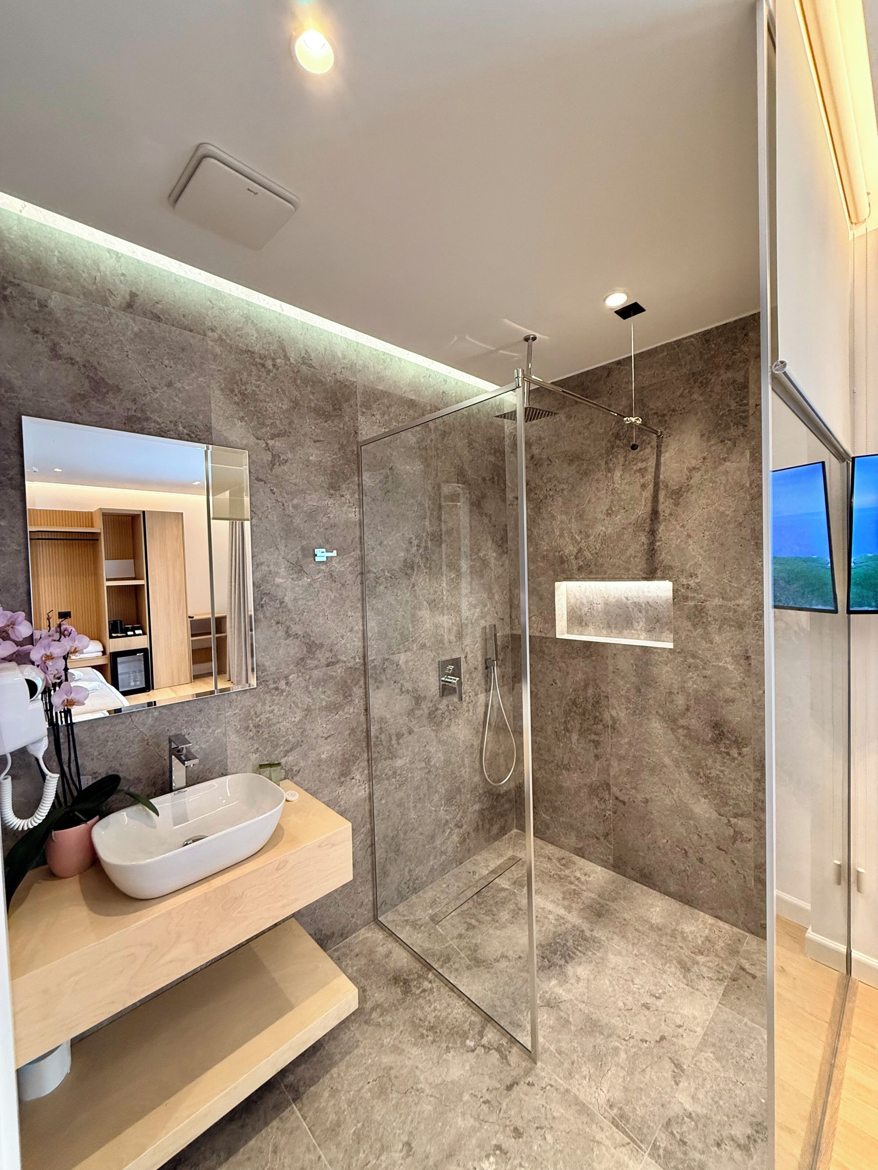 Un baño moderno con ducha envuelta en vidrio, un espejo grande y un mueble de tocador de madera.
