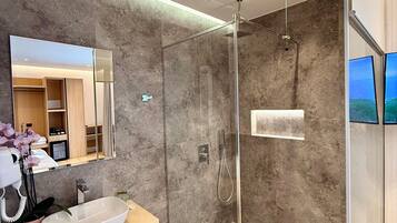 Un baño moderno con ducha envuelta en vidrio, un espejo grande y un mueble de tocador de madera.