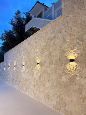 A stone wall with embedded lighting fixtures, a flat roof, and a clear sky. - Marisol Hotel (Sarandë)