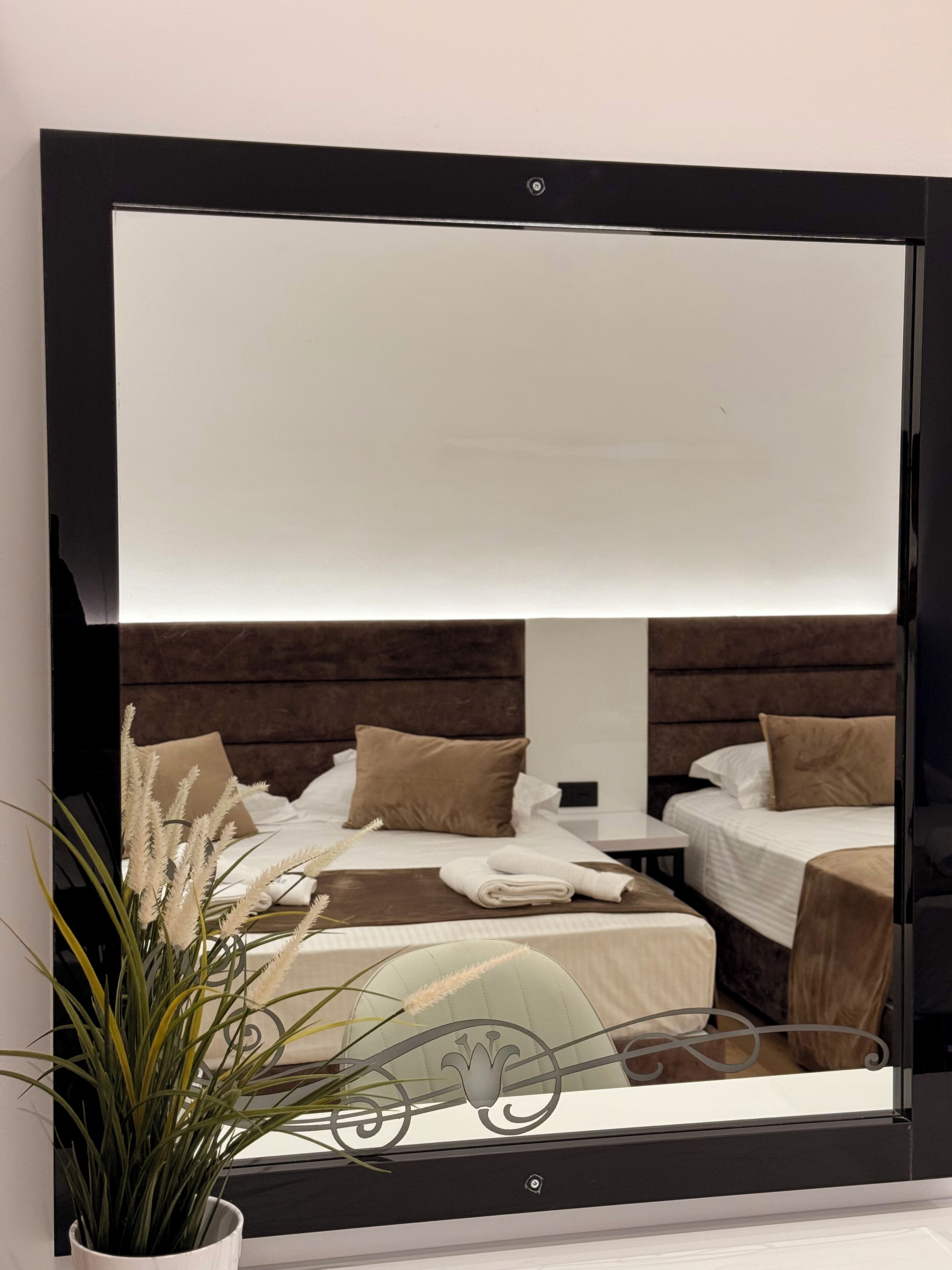 A large mirror reflecting a bedroom with a bed, pillows, and a bedside table.