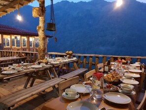 Ein Essbereich mit Holztischen und -bänken, umgeben von einem Holzzaun, mit Blick auf eine Berglandschaft.