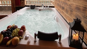 Een houten chalet met een jacuzzi, een fruitmand en uitzicht op bergen.