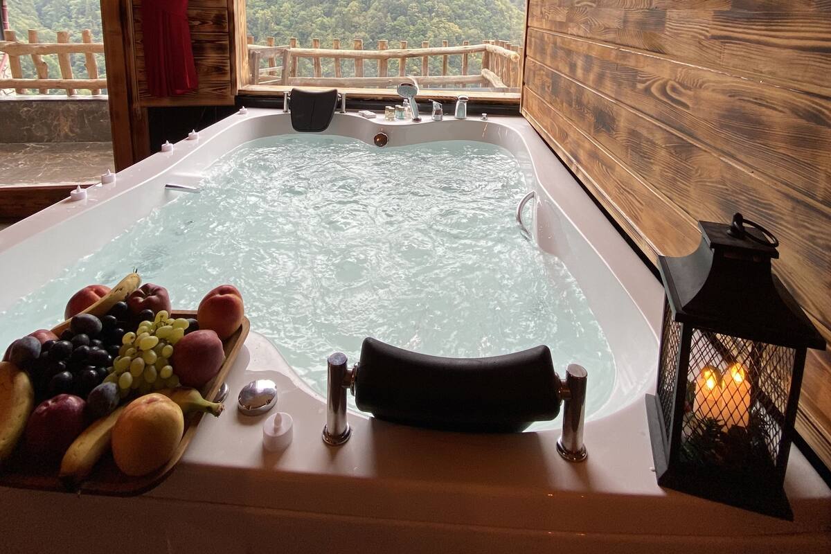 Una cabaña de madera con jacuzzi, cesta de frutas y vistas a las montañas.