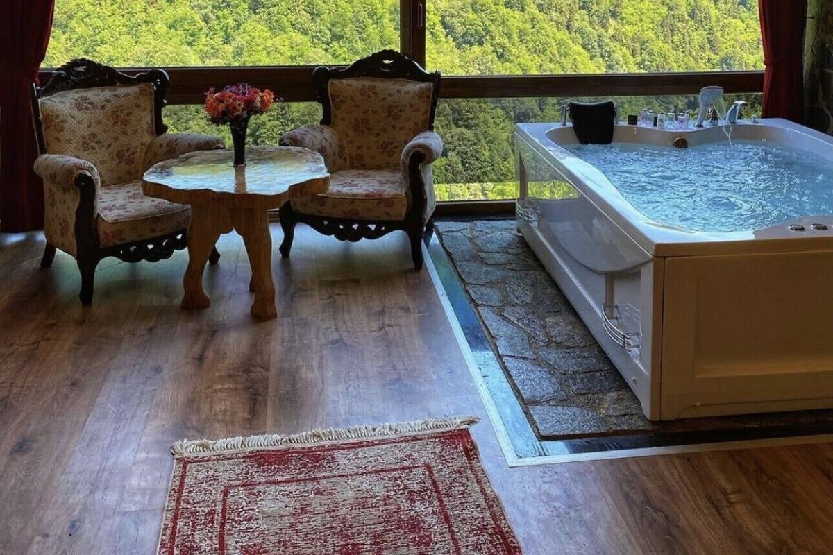 Un interior de madera con un ventanal grande, dos sillones tapizados, una mesita y una alfombra roja, además de un jacuzzi.