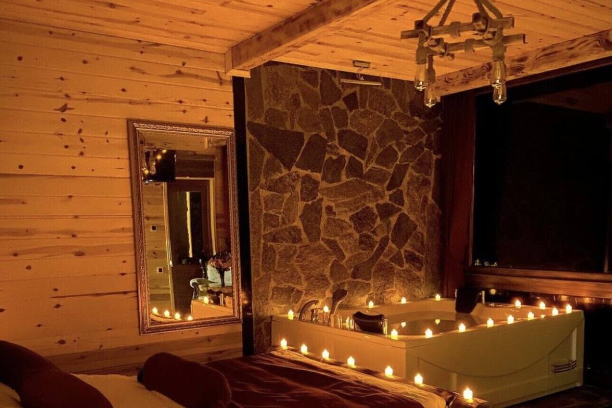 Una habitación acogedora con pared de piedra, un espejo grande, una cama de madera y una bañera con velas.