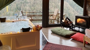 Een knus vakantiehuisje met een jacuzzi, een open haard en een groot raam met uitzicht op een bebost gebied.