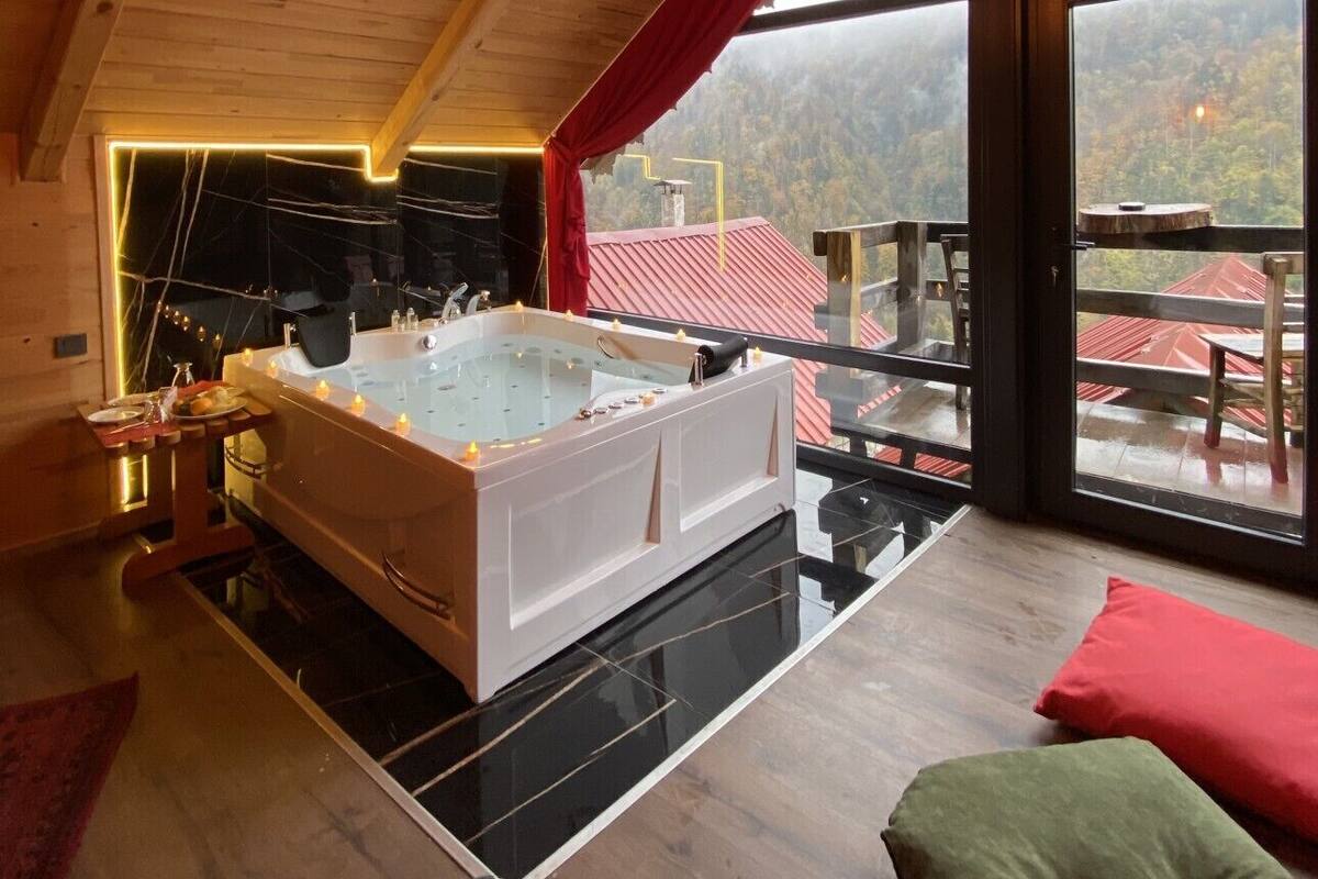Un interior moderno con una bañera grande, techo de madera y vistas a un paisaje montañoso.