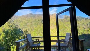 Een houten terras met twee gestreepte stoelen met uitzicht op een bebost berglandschap.