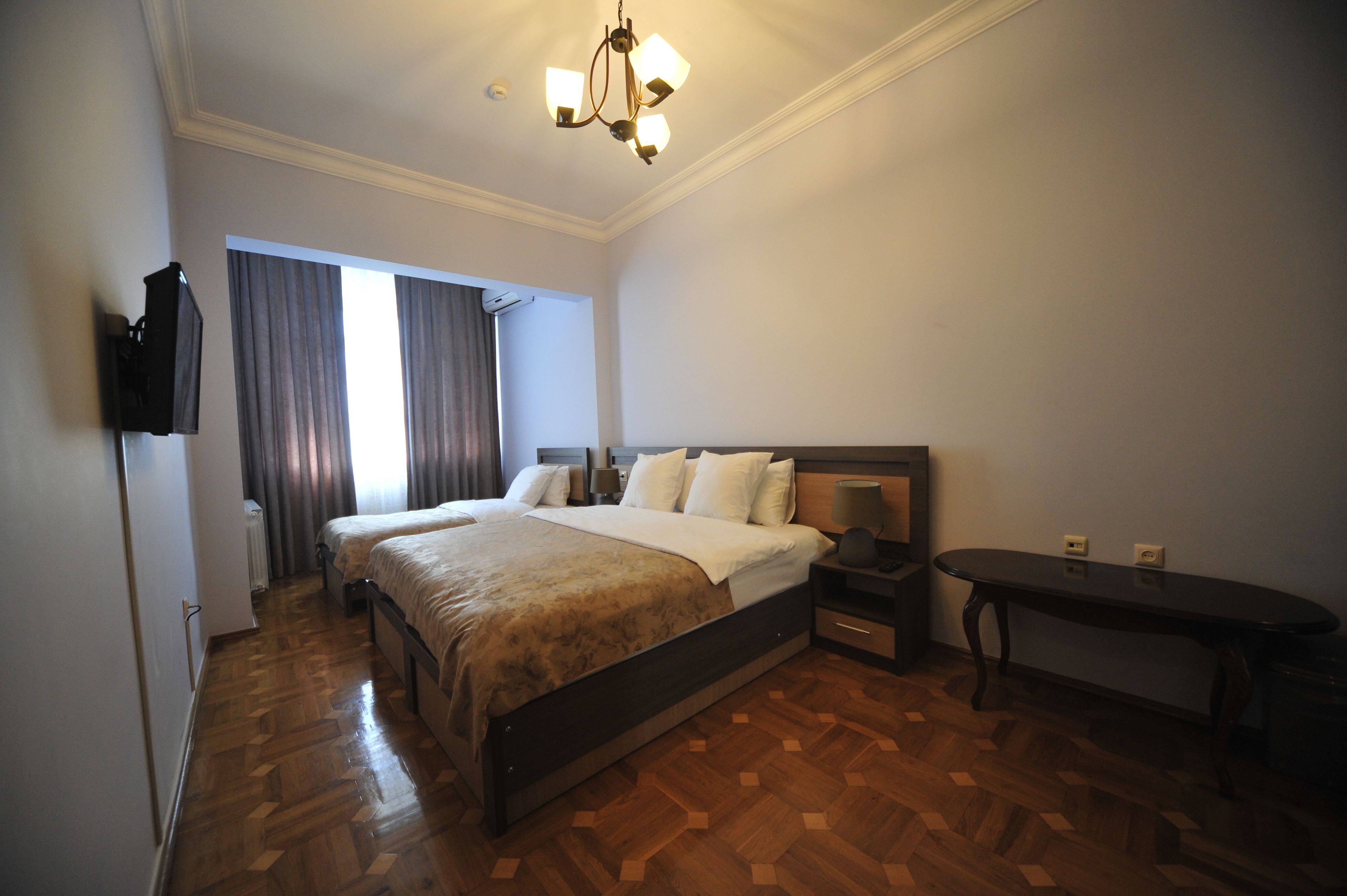 Una habitación de hotel con una cama grande, una mesita de noche, un escritorio y un televisor fijado a la pared.