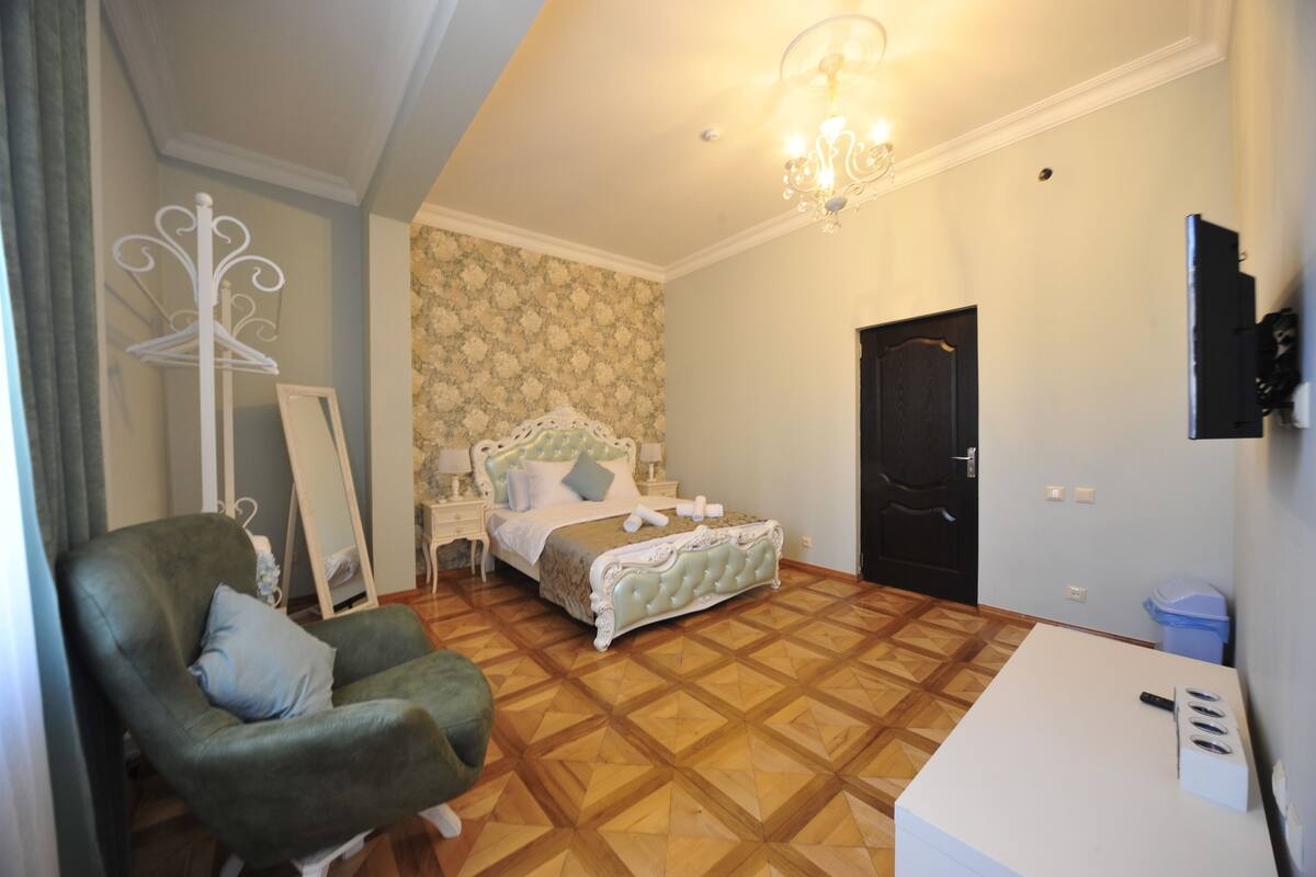 Ein Schlafzimmer mit einem Bett, einem Sessel, einem Schminktisch, einem Spiegel und einer Tür.