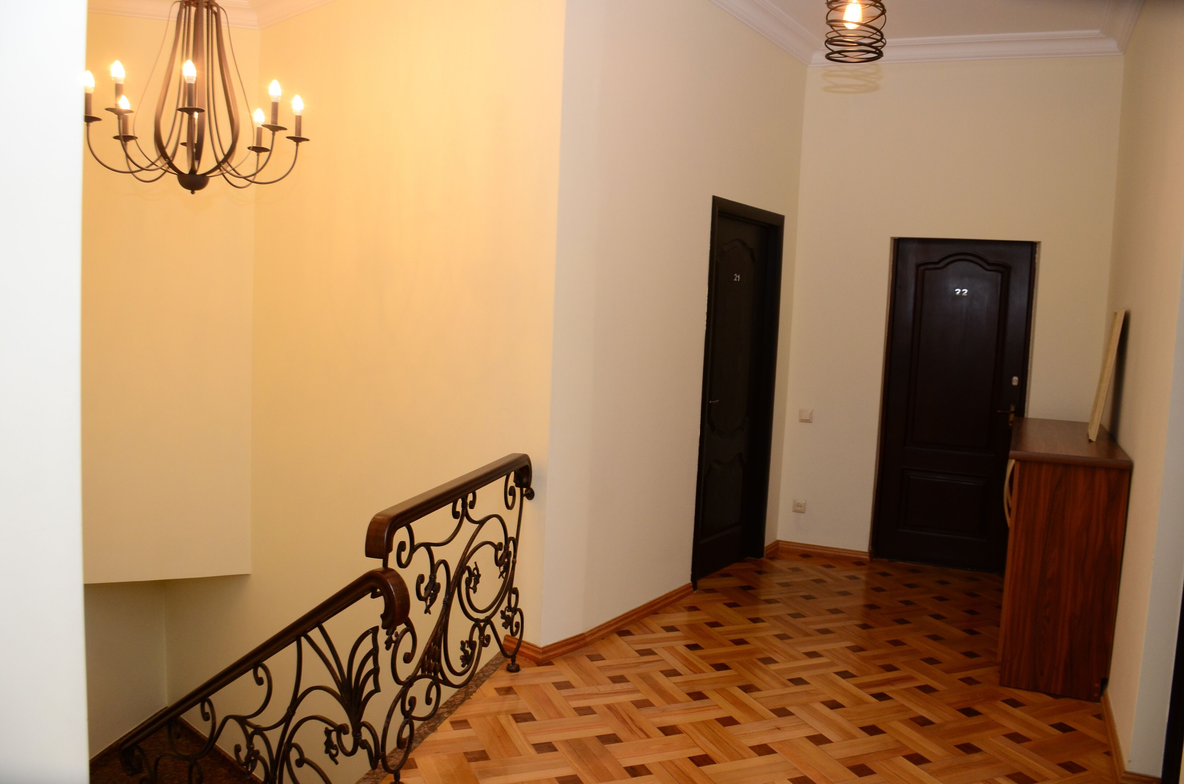 Un pasillo con suelo de parqué de madera, barandilla de metal negro y un candelabro.