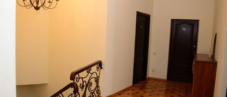 Un pasillo con suelo de parqué de madera, barandilla de metal negro y un candelabro.