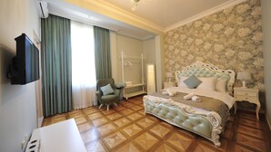 A bedroom with a large bed, a chair, a TV, and a wooden floor. - Guest House Batumi Globus (Batumi)