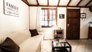 A cozy living room with a sofa, a glass coffee table, a wooden door, and a window with curtains.
