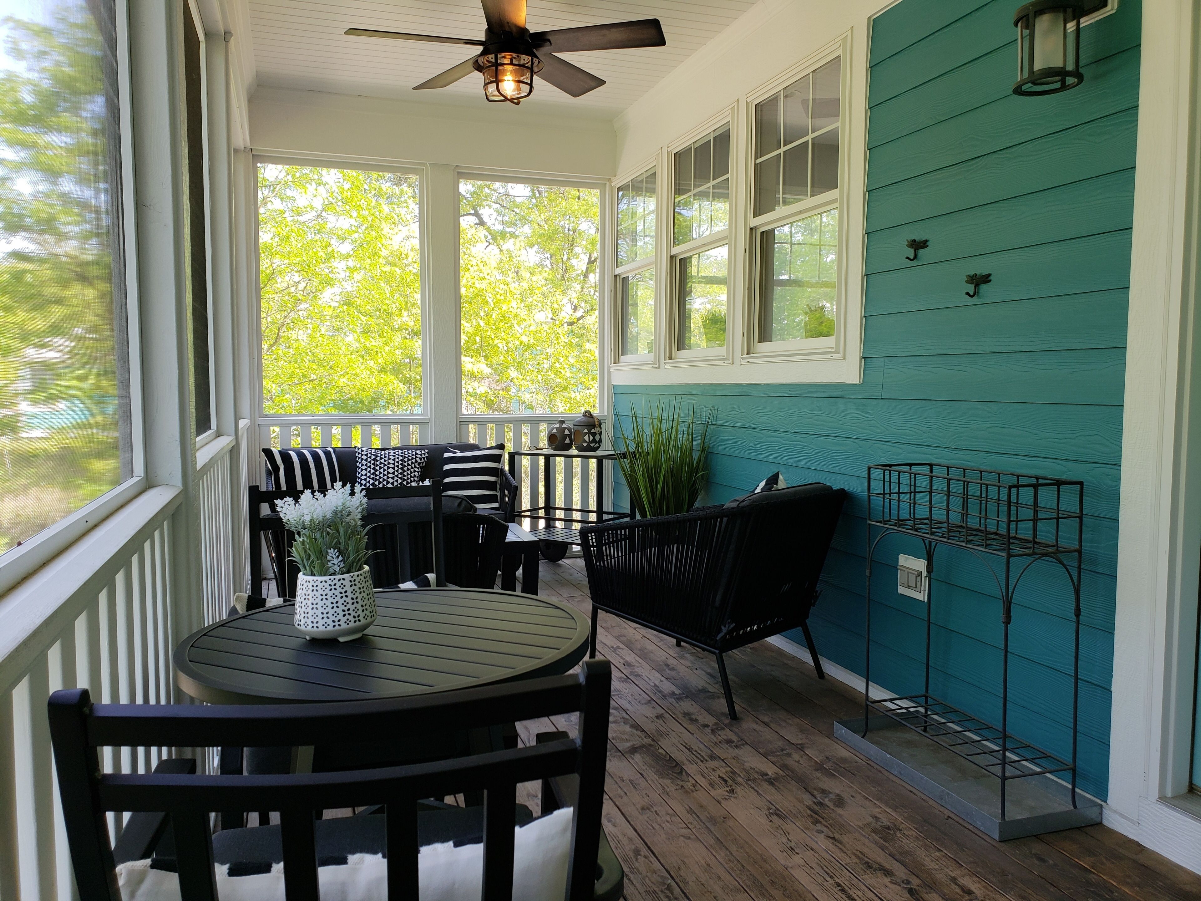 A covered porch with a ceiling fan, a round table with chairs, and a potted plant.