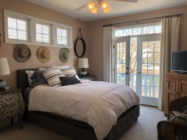A bedroom with a bed, two bedside tables with lamps, a television on a wooden cabinet, and a balcony door. - Steps to everything! The Cape Codder at Beachwalk Resort w/ Water Views (Michigan City)