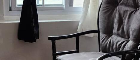 A room with a window, a chair, and a view of a red building outside.