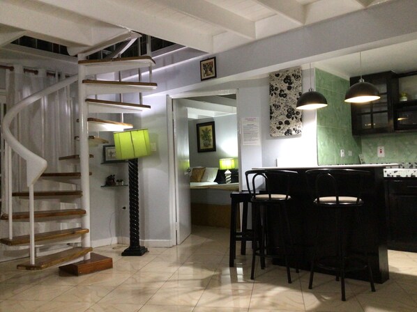 A modern kitchen with a spiral staircase, a dining area with bar stools, and a green tiled backsplash. - Mystic Ridge Paradise 2 bedroom Penthouse Condo (Comfy and Relaxing) (Ocho Rios)
