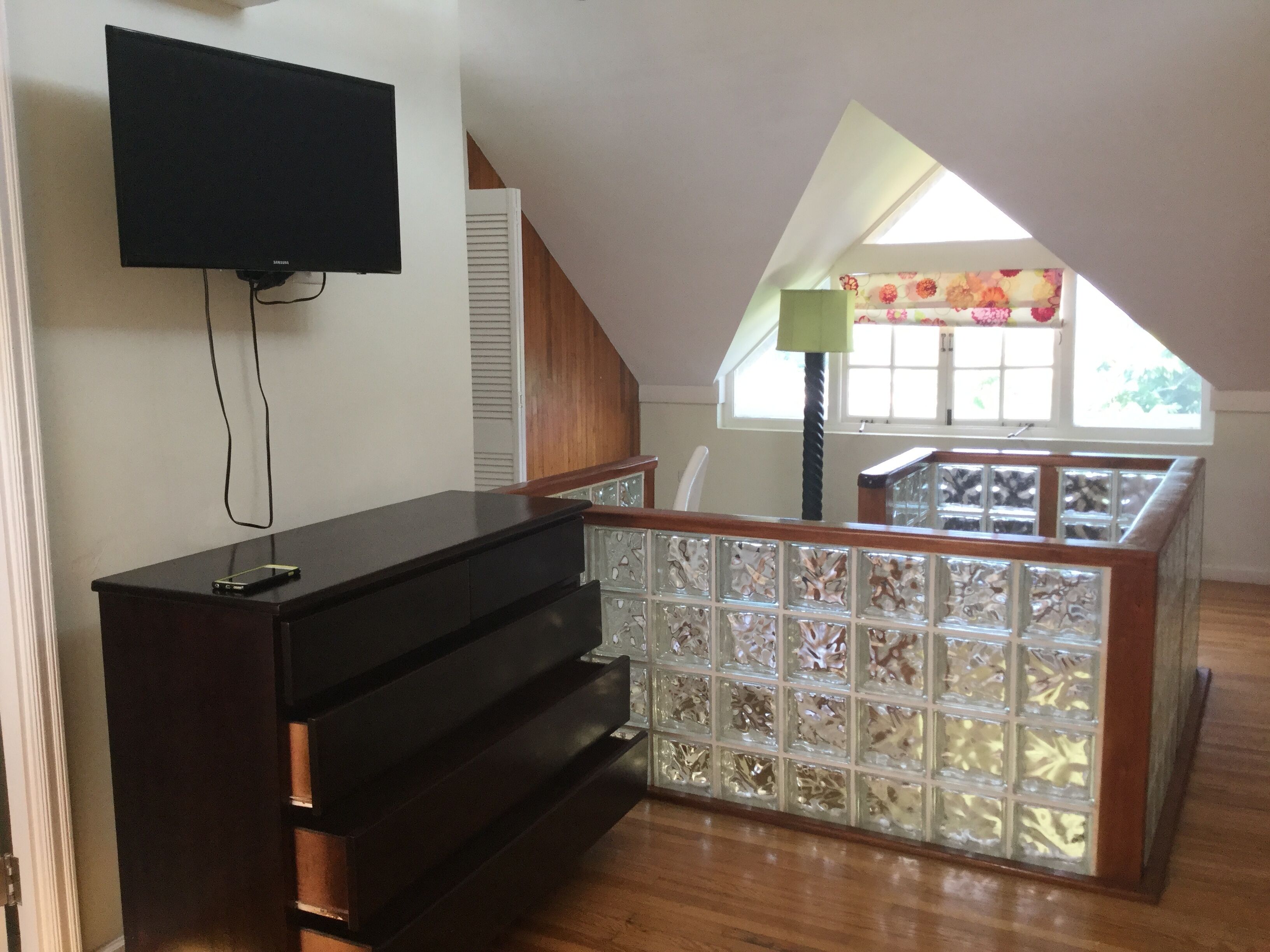 Een kamer met een aan de muur bevestigde televisie, een trap naar een balkon en een decoratieve glazen scheiding.